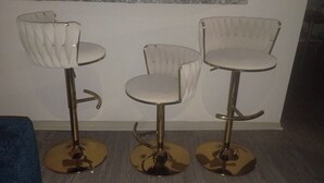 Trois tabourets de bar, dotés d’un haut dossier et d’une base dorée, sont placés contre un mur.