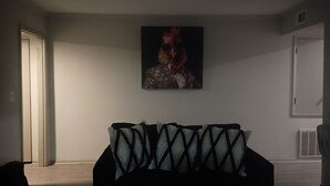 Une pièce avec un lit, une porte, un tableau accroché au mur et une bouche d’aération.