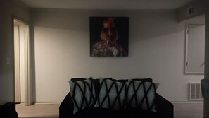 Una habitación con cama, una puerta, un cuadro en la pared y una rejilla de ventilación.