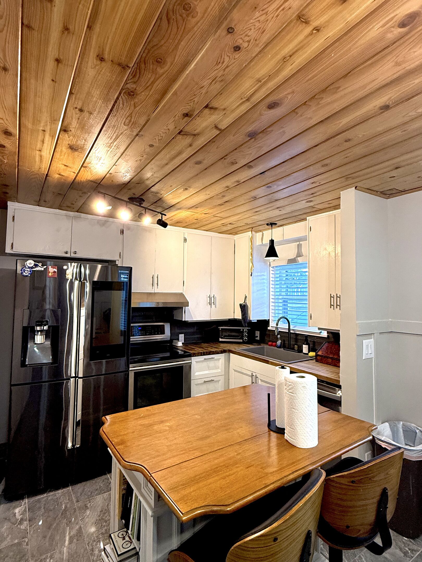A kitchen with wooden ceiling, stainless steel appliances, white cabinets, and a wooden table.
