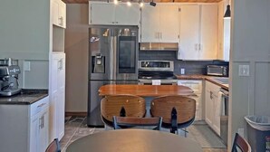 A modern kitchen with wooden ceiling, stainless steel appliances, a round dining table, and two chairs.
