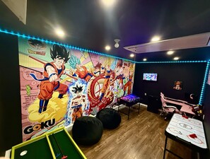 Una habitación con un mural grande de temática anime, mesa de fútbol de mesa, puffs y televisor.