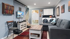 A compact living space with a sofa, a TV, a bookshelf, a desk, and a washing machine.