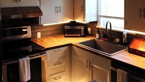 A kitchen with wooden ceiling, white cabinets, a black stove, and a window with blinds.