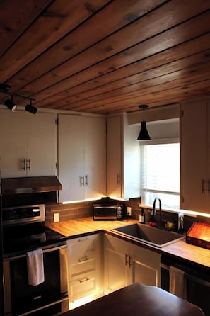 A kitchen with wooden ceiling, white cabinets, a black stove, and a window with blinds.