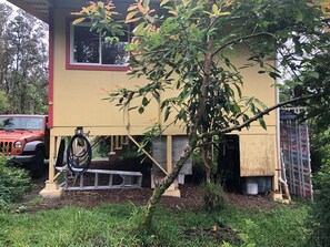 A yellow building with a window, a tree in front, and a red vehicle parked nearby. - Off-the-Grid Cottage in a Remote Big Island Village (Pāhoa)