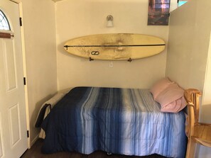 A bedroom with a bed, a surfboard mounted on the wall, and a door. - Off-the-Grid Cottage in a Remote Big Island Village (Pāhoa)