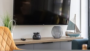 Uma sala de estar moderna com televisão de tela plana, um pequeno veleiro decorativo e um vaso com planta.