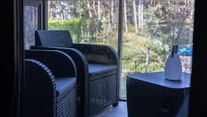 Varanda com sofá de vime e uma mesa pequena, com vista para uma área arborizada.