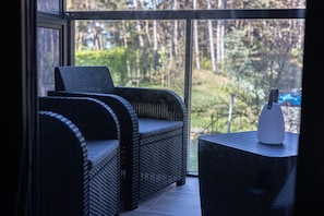 Ein Balkon mit einem Korbssessel, einem kleinen Tisch und Blick auf ein bewaldetes Gebiet.