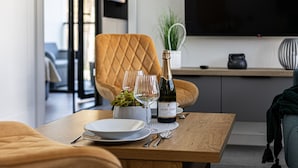 Uma área de refeições com uma mesa de madeira, dois copos de vinho, uma garrafa de vinho e um vaso com planta.