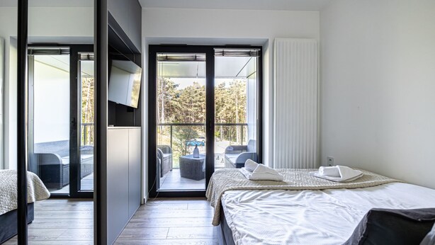 Quarto de hotel moderno com uma cama, uma varanda com mobiliário exterior e uma porta deslizante para a varanda.