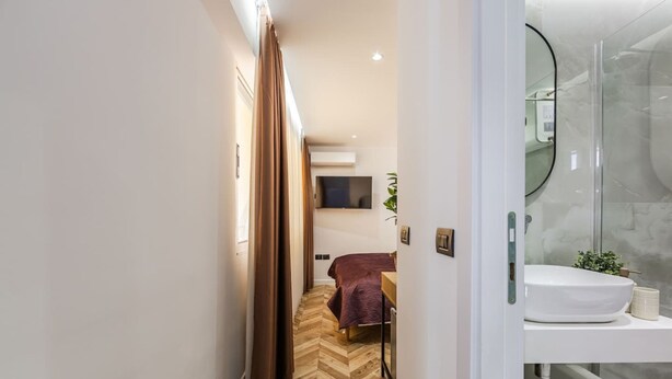 A hotel room with a herringbone floor, a bed with a purple bedspread, a mounted TV, and a bathroom with a glass shower enclosure. - Konak Lemon Guesthouse Heart of Vlora (Vlorë)