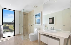 A modern bathroom with a glass shower enclosure, a toilet, a sink with a mirror, and a view of a golf course through a large window.