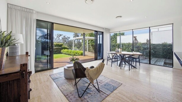 A modern interior with a dining area, a seating area with a chair, and large glass doors leading to an outdoor space. - L&L Golfside Retreat (Benowa)