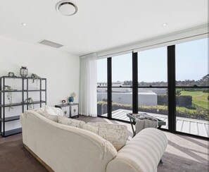 A modern living room with a large window, a sofa, a side table, and a bookshelf.