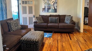 Un salon avec un ensemble de canapés marron, des coussins à motifs, un plancher en bois, un ventilateur de plafond et une porte dotée de panneaux en verre dépoli.