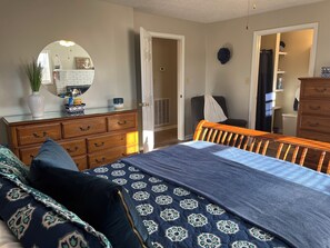 A bedroom with a bed, dresser, mirror, and a door leading to another room.