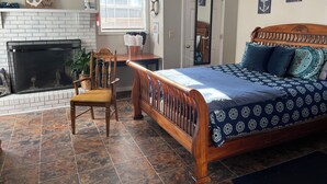 Une chambre à coucher avec un lit en bois, une cheminée, un fauteuil et une fenêtre.