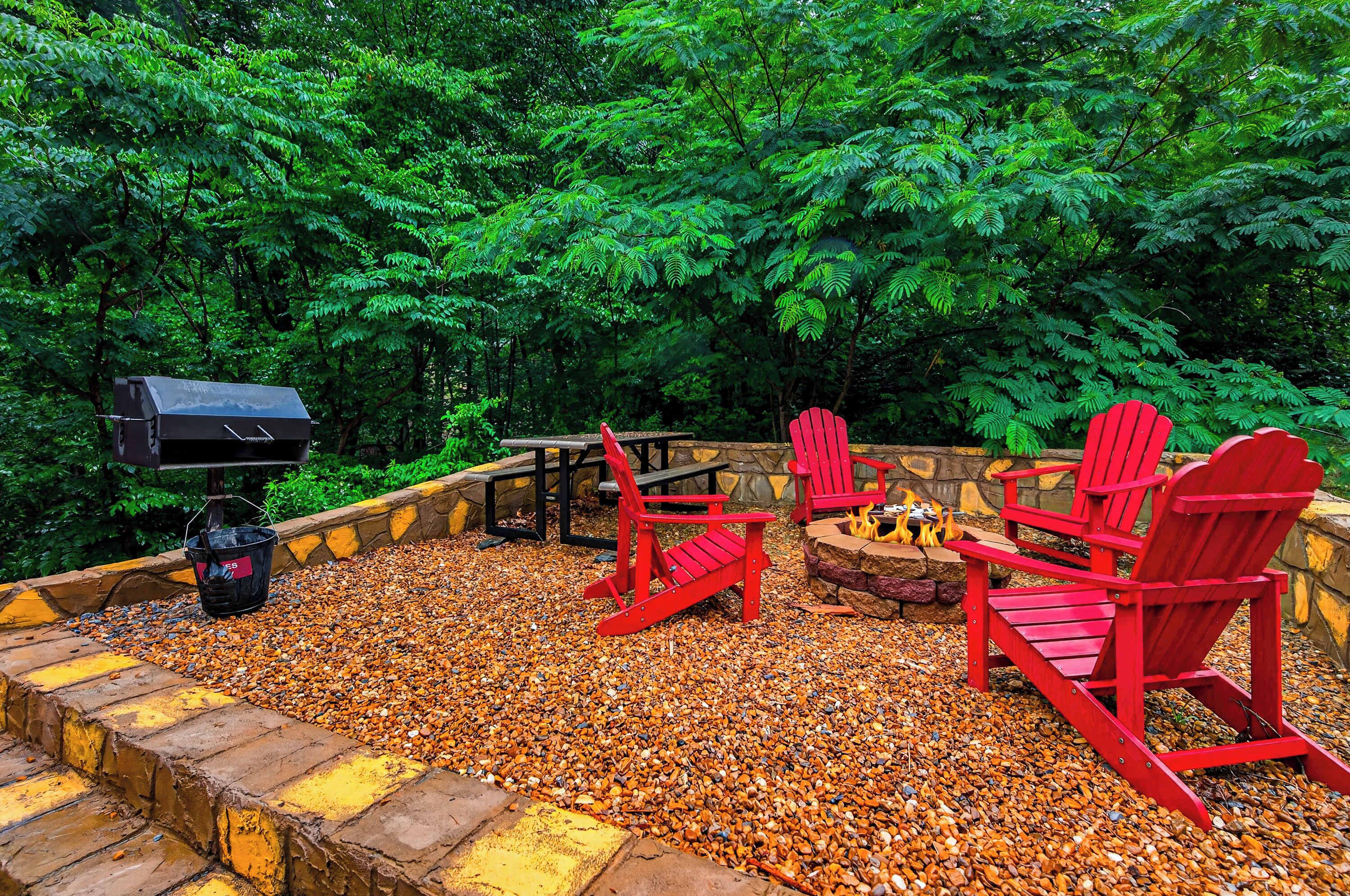 An outdoor seating area with red Adirondack chairs, a fire pit, and a grill.