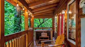 Une véranda en bois offrant une vue sur la verdure, un jacuzzi et des chaises en bois.