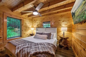 Ein Schlafzimmer einer Holzhütte mit Bett, Deckenventilator und zwei Fenstern.