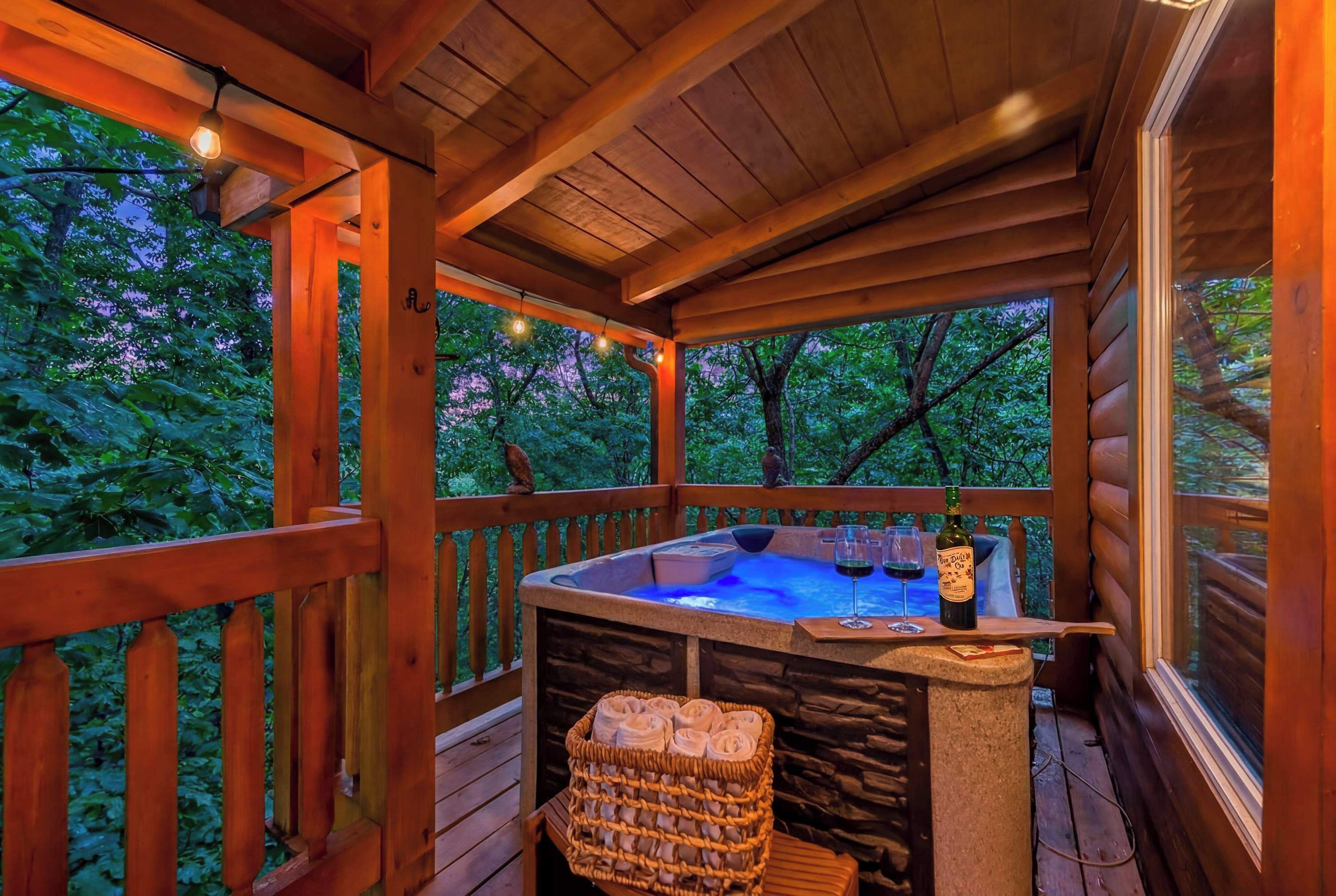 Une terrasse en bois avec un jacuzzi, un banc en pierre et un panier rempli de serviettes.