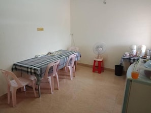A dining area with a table, chairs, a fan, and a small stool. - Mangkonlay Hostel (Tha Phae)