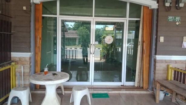 Entrada de hotel com porta de vidro, dois bancos brancos e uma mesa redonda.