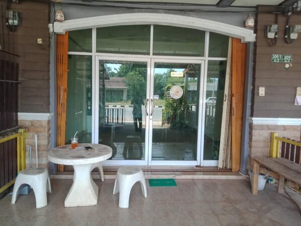 A hotel entrance with a glass door, two white stools, and a round table.