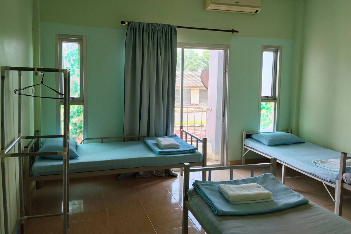 A room with two beds, a window, an air conditioning unit, and a curtain.