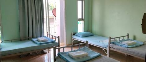 A room with four single beds, a window, and a door leading outside.