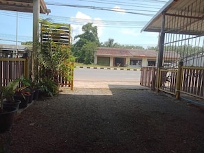 A gated entrance with a gravel path leading to a building with a tiled roof. - Mangkonlay Hostel (Tha phe)