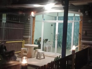 A room with a glass door leading to a balcony, a small round table, two white stools, and a lantern. - Mangkonlay Hostel (Tha phe)