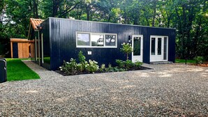 A modern, single-story building with a gravel driveway, a small garden, and a wooden structure in the background.