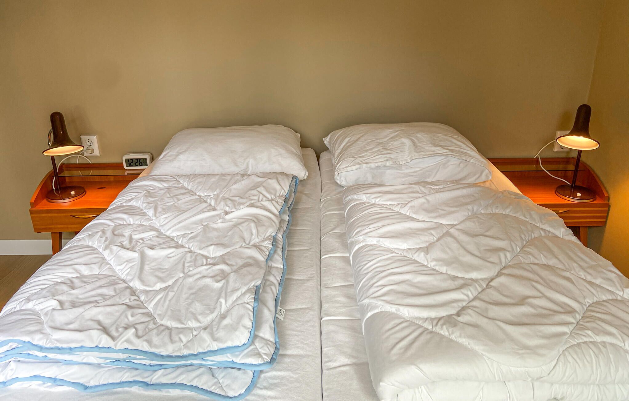 A twin room with two single beds, each with a nightstand, a lamp, and a digital clock.