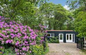 Un bâtiment avec une allée gravillonnée, entouré d’une végétation luxuriante et d’arbustes en fleurs.