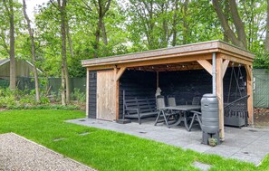 Un espace extérieur abrité, aménagé avec une table et des chaises, un distributeur d’eau et un barbecue.