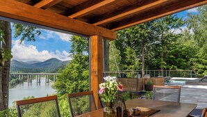Una terraza de madera con una mesa y sillas, con vista a un río y montañas.