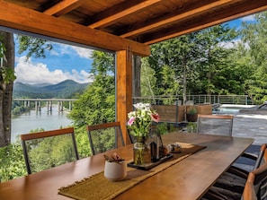 Eine Holzterrasse mit Tisch und Stühlen mit Blick auf einen Fluss und Berge.