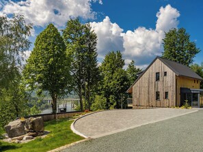 Ein modernes Holzhaus mit einer gewundenen Auffahrt, umgeben von üppigem Grün und blauem Himmel.