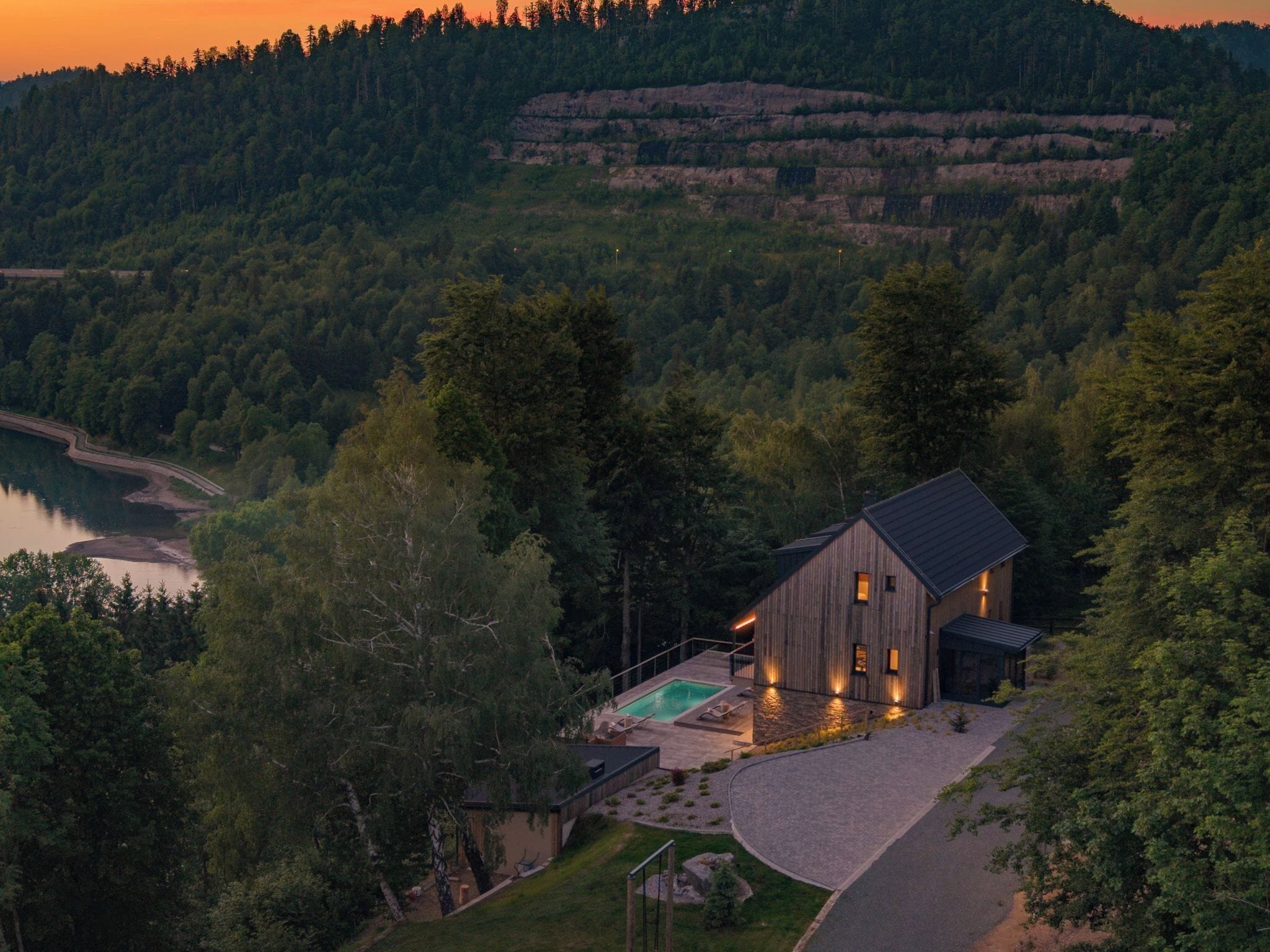 A modern house with a swimming pool, surrounded by dense forest and hills.