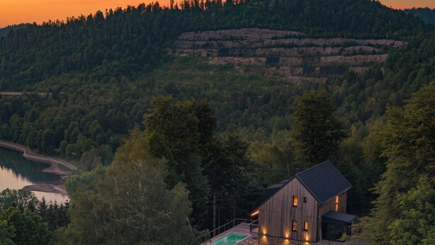 Una casa moderna con piscina, rodeada de un bosque frondoso y colinas.