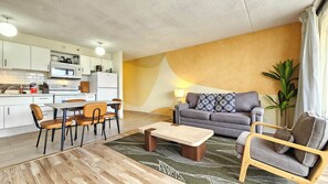A modern living room with a sofa, coffee table, and chairs, adjacent to a kitchen with white cabinets and appliances. - Cozy 1-bedroom apartment in wonderful Honolulu with AC (Honolulu)