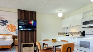 Une cuisine moderne avec des appareils électroménagers blancs, un coin repas avec une table et des chaises, et un téléviseur fixé sur un panneau en bois.