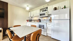 A modern kitchen with white cabinetry, a built-in microwave, a stove, and a refrigerator. There is a dining table with chairs and a television mounted on the wall. - Cozy 1-bedroom apartment in wonderful Honolulu with AC (Honolulu)