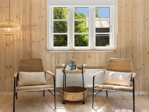 Zwei Korbstühle mit Kissen, ein Korbtisch mit einer Vase und ein Fenster mit Blick auf Bäume.