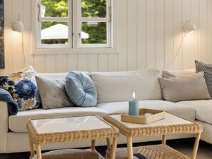 Ein Zimmer mit einer gestreiften Couch, einem kleinen Tisch, einer brennenden Kerze und einem Fenster mit Blick auf Grünflächen.