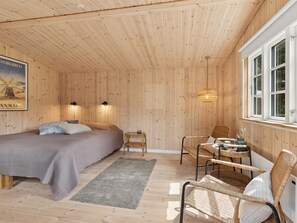 Ein Zimmer mit einem Bett, einem Sessel, einem kleinen Tisch, einem Teppich und einem Fenster.