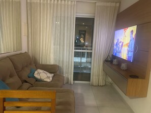 Sala de estar com sofá, televisão e vista através de uma porta de vidro.